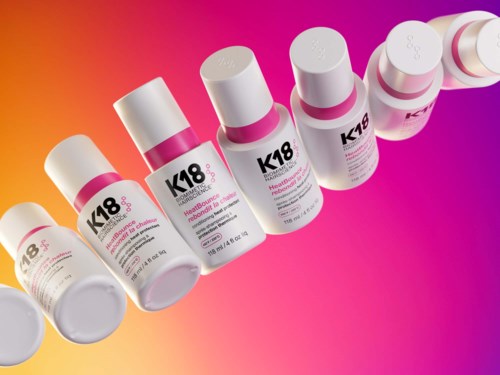 Multiple bottles of K18 hair treatment line against a colorful background. Each bottle has a white cap and pink accents.