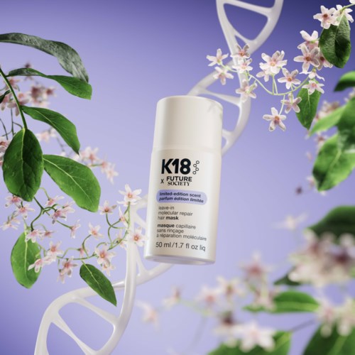 A white bottle labeled 'K18' floats among green leaves and pink flowers on a light purple background.