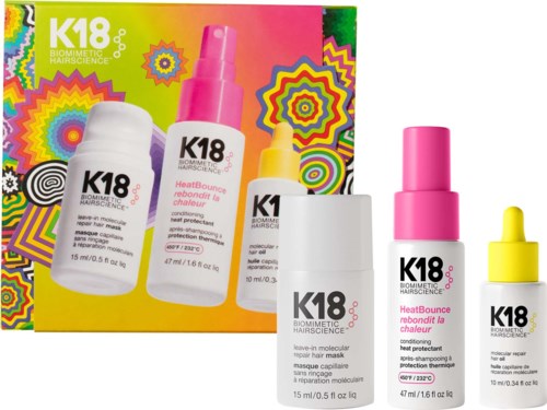 Box with four hair care bottles in pink, white, and yellow, featuring K18 branding and colorful geometric background.