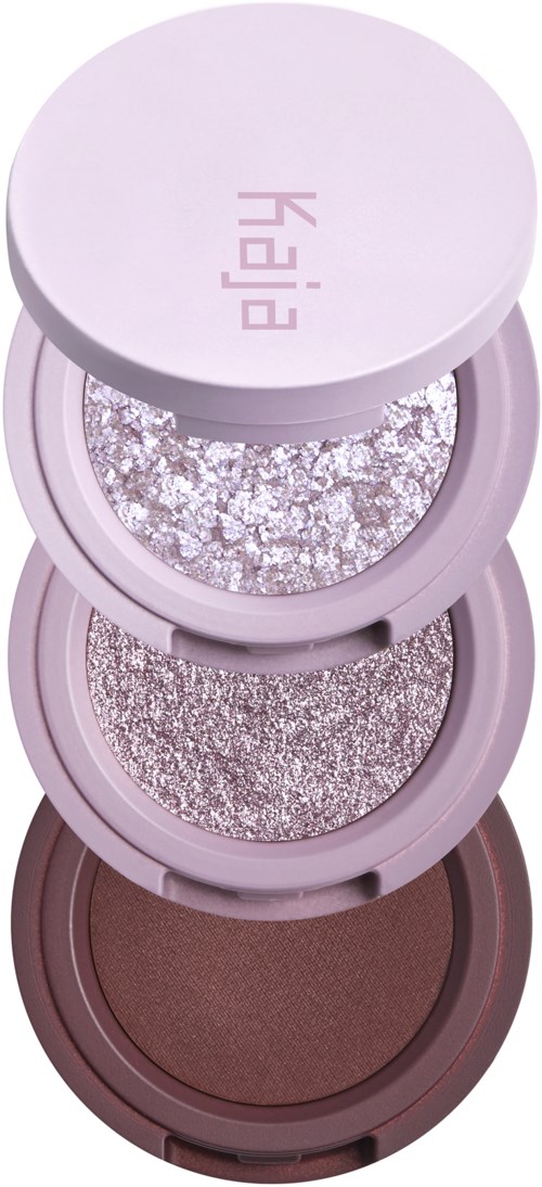 Drei runde Behälter mit glitzernden Lidschatten in Silber-, Grau- und Brauntönen. Der obere Deckel ist helllila mit Kai.