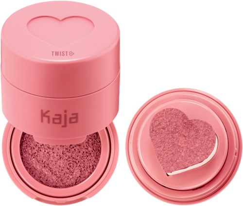Ronde roze container met een hartvormig gat, gemarkeerd 'Kaja', en een hartvormige spons erin. Compact en schattig.