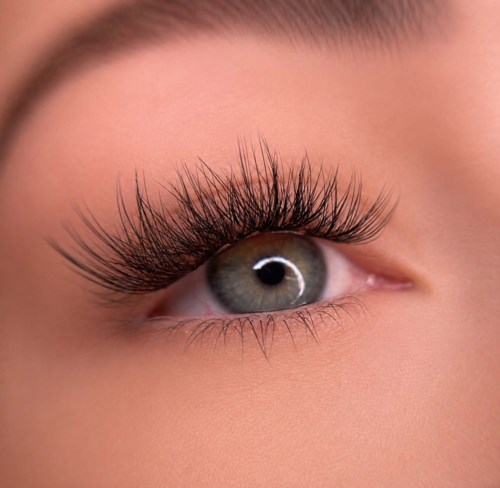 Close-up of a woman's eye with long, thick eyelashes and gray-green iris.