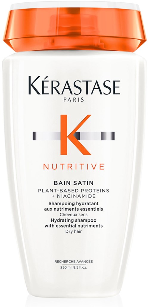 Een witte fles met oranje deksel, labelt Kérastase Nutritive Bain Satin voor droog haar, bevat plantaardige eiwitten.