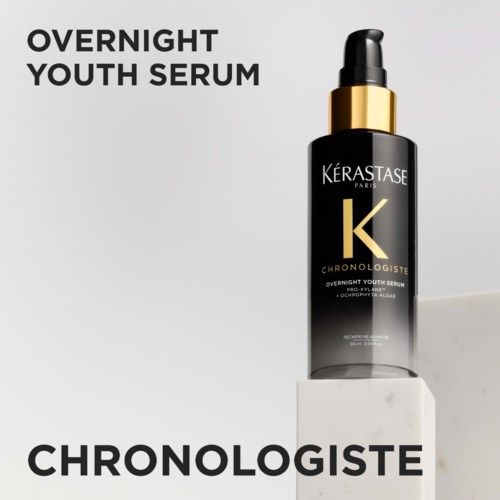 Een zwarte fles met gouden dop en pipet voor Overnight Youth Serum van Kérastase, weergegeven op een witte blok.
