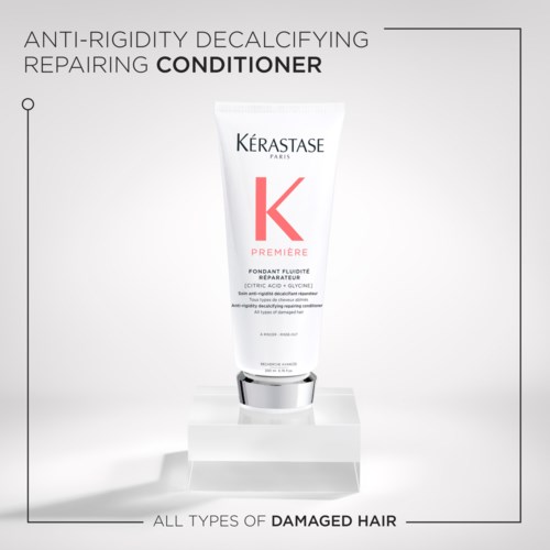 A white tube of Kérastase conditioner for damaged hair, with red and black text, stands on a clear platform.