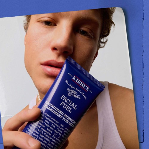 Ein junger Mann hält eine blaue Tube mit Gesichtspflegecreme in der Nähe seines Gesichts.