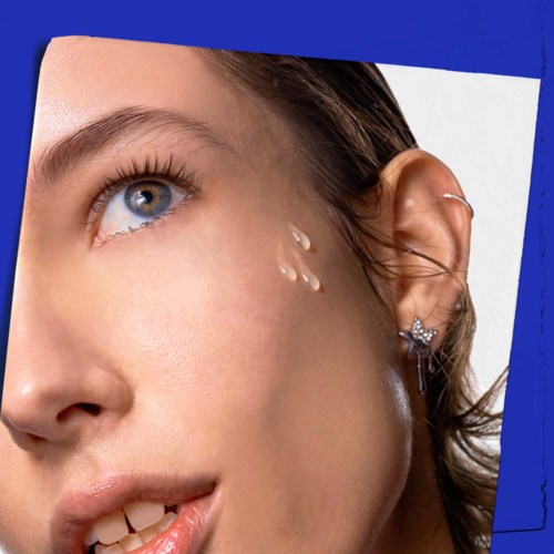 Close-up of a woman with tears on her cheek and blue eyes, wearing earrings, and looking upwards.