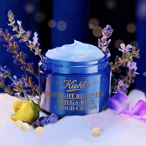 Een potje Kiehl's Midnight Recovery Omega-Rich Cloud Cream, omringd door lavendel, een gele bloem en paarse bloemen.