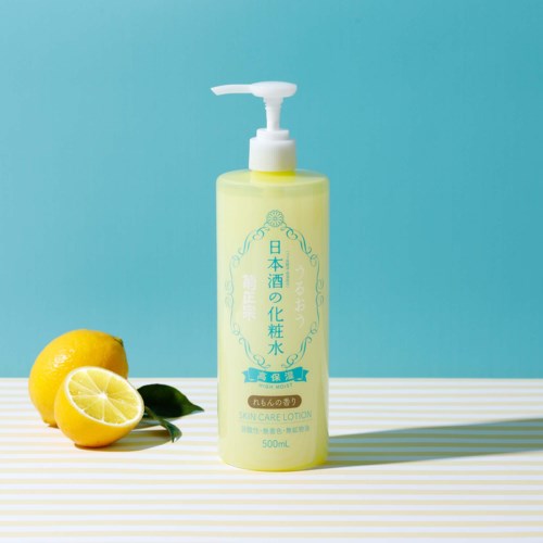 A light yellow skin care lotion bottle with Japanese text, a pump top, placed on a striped surface with lemons nearby.