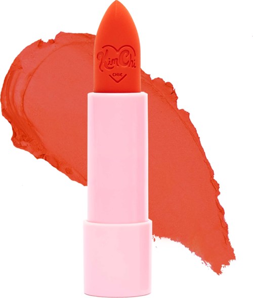 A pink lipstick with a peach-colored cap and a heart-shaped logo, with a red-orange smear behind it.