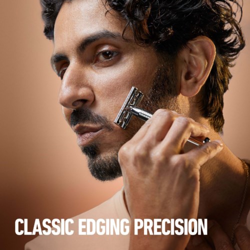Ein Mann mit lockigem Haar rasiert sein Gesicht mit einem Safety-Rasierer, Nahaufnahme. Text lautet "Classic Edging Precision."