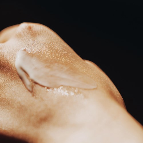Close-up van een gezicht met huidverzorgingsproduct op wang, benadrukt gladde huid en heldere textuur.