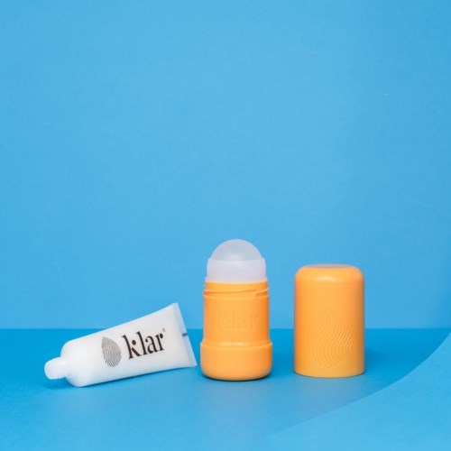 Een witte lipbalsemtube, een gele container met deksel en een lege gele dop op een blauwe achtergrond.