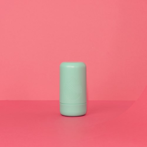 Een pastelgroen cilindervormig voorwerp staat op een roze achtergrond, met een subtiel patroon op het oppervlak.