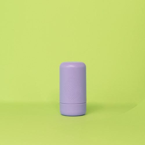 A purple cylindrical object stands on a green background; it appears to be a small, smooth device or container.