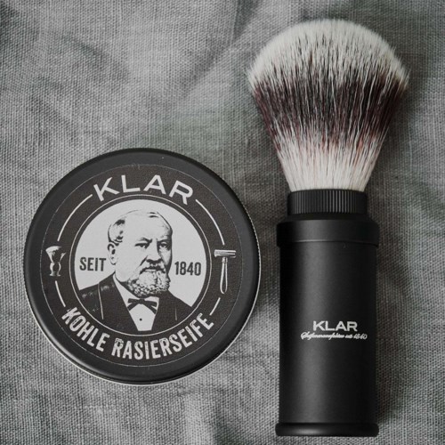 A shaving soap container and a shaving brush on a gray fabric background.