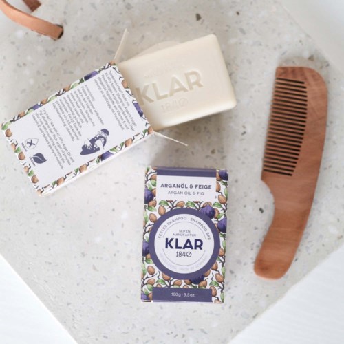 Soap, shampoo, and a wooden comb on a white surface.