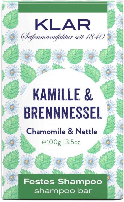 A shampoo bar packaging with green leaves and white flowers, labeled with brand Klar, chamomile, and nettle ingredients.