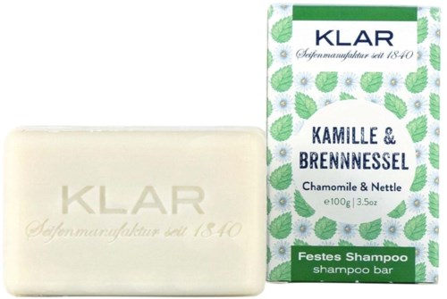 Bar of soap with herbal scent beside packaging featuring leaves and flowers, labeled as shampoo bar and natural ingredients.