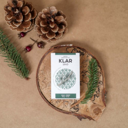 A gift box, pine cones, small red berries, and pine branches arranged around a round wooden slice.