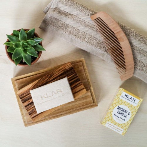 A small green succulent plant, a wooden comb, a wooden tray with soap, and a honey and vanilla candle.