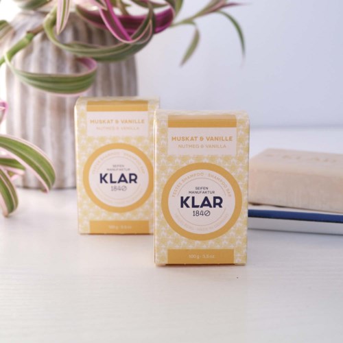 Two small boxes labeled 'Klar 1840' with vanilla scent, placed on a white surface with plants and books nearby.