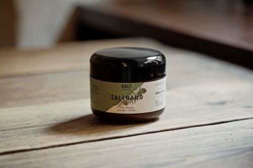 Ein kleiner schwarzer Behälter mit weißem Etikett steht auf einer Holzoberfläche, wahrscheinlich ein Kosmetik- oder Pflegeprodukt.