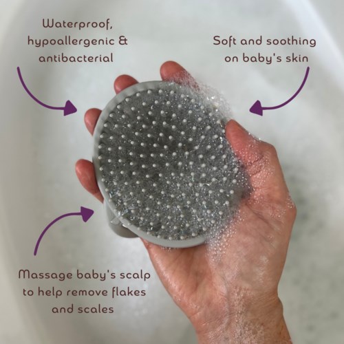 A hand holding a silicone brush, labeled as waterproof, gentle for baby's skin, used for scalp cleaning.