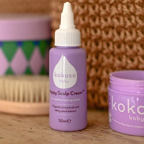 A small purple bottle labeled 'Happy Scalp Cream' with a drop icon, beside a matching purple container and a brush.