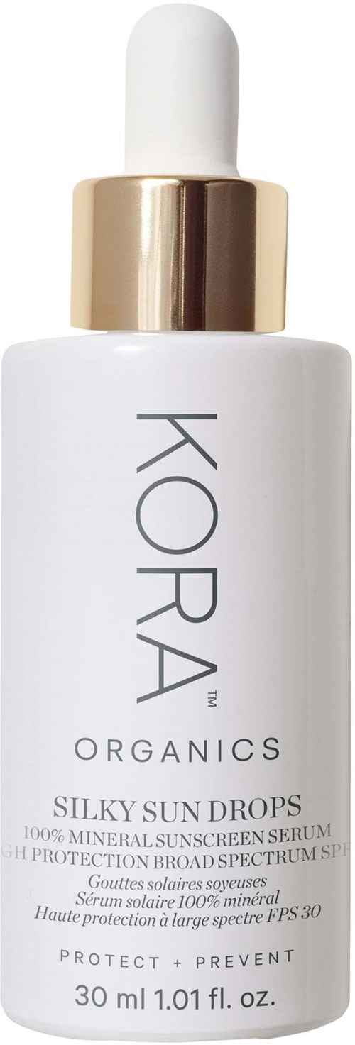 Eine weiße Flasche mit Goldkappe, beschriftet 'KORA ORGANICS' und 'SILKY SUN DROPS' zum Sonnenschutz.