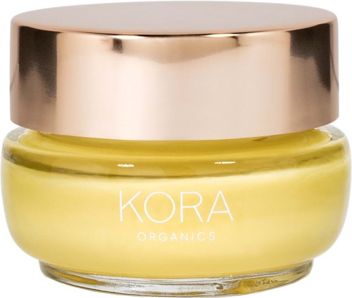 Kleines Glas mit gelber Creme und einem glänzenden, goldfarbenen Deckel. Das Etikett sagt "KORA ORGANICS."