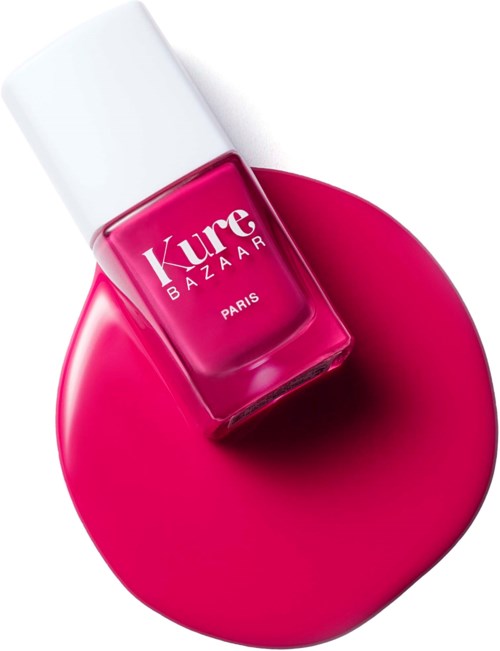Eine pinkfarbene Nagellackflasche auf einer passenden pinken Oberfläche. Weißer Deckel, Marke 'Kure Bazaar' aus Paris.