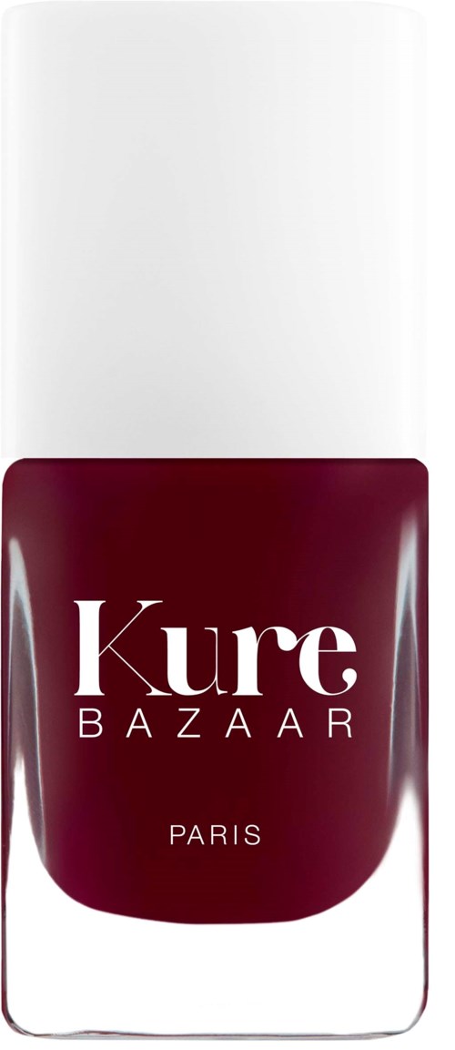 Eine Flasche Kure Bazaar Nagellack, dunkelroter Farbe, mit weißem Deckel und klarem Etikett mit schwarzem Text.