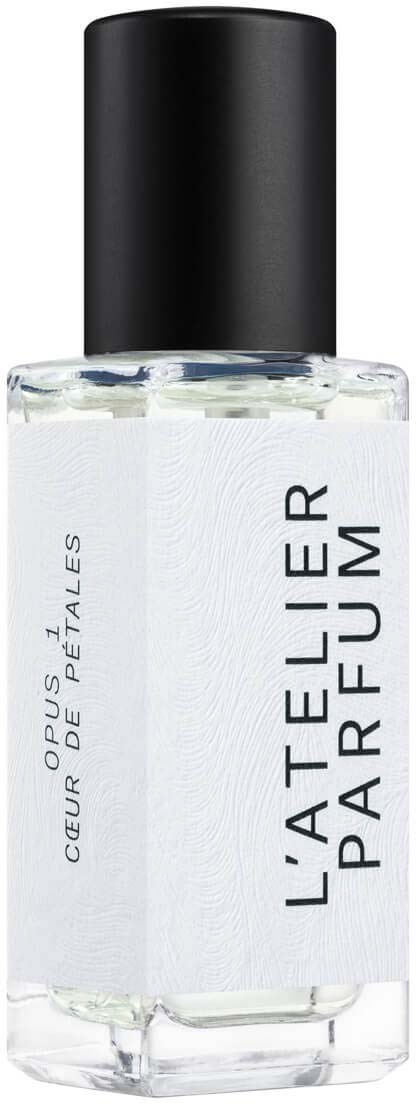 A clear perfume bottle with a black cap and white label that says "L'Atelier Parfum" and "Coeur de Pétales."