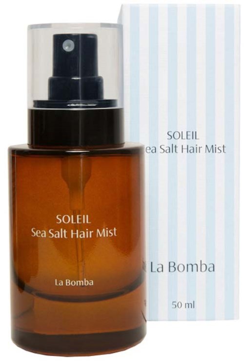 En brun flaske med Soleil Sea Salt Hair Mist med svart sprayhode og klar lokk, ved siden av en stripet eske.