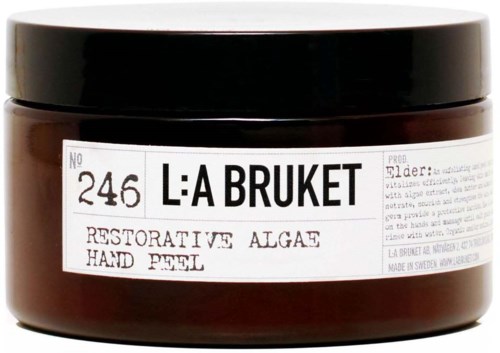 Een pot met La Bruket-label, met rustgevende algen-handscrub, zwarte deksel en witte label, tegen een zwarte achtergrond.