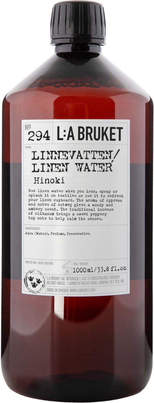 Eine braune Flasche mit schwarzem Deckel, hat ein weißes Etikett mit Text, darunter 'L: A BRUKET' und 'LINEN WATER Hinoki'.