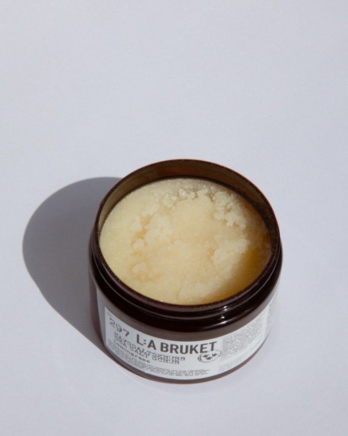 Ein brauner Behälter mit der Aufschrift 'LÅ BRUKET' enthält eine cremige, blassgelbe Substanz, wahrscheinlich ein Hautpflegeprodukt oder Körperbutter.
