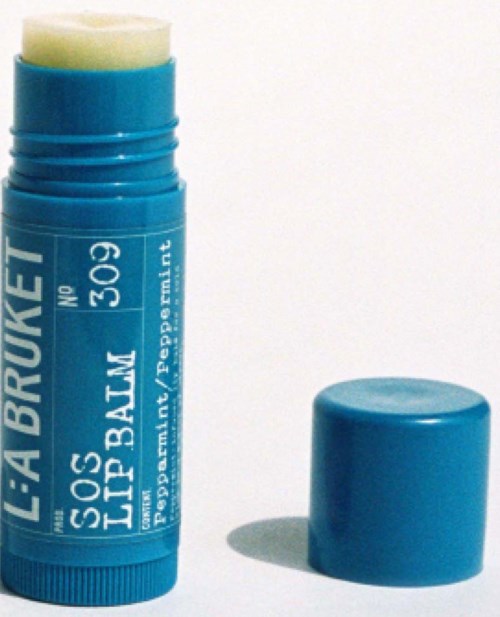 Blauer Lippenbalsamstift mit weißem Text und Deckel daneben auf weißem Hintergrund.