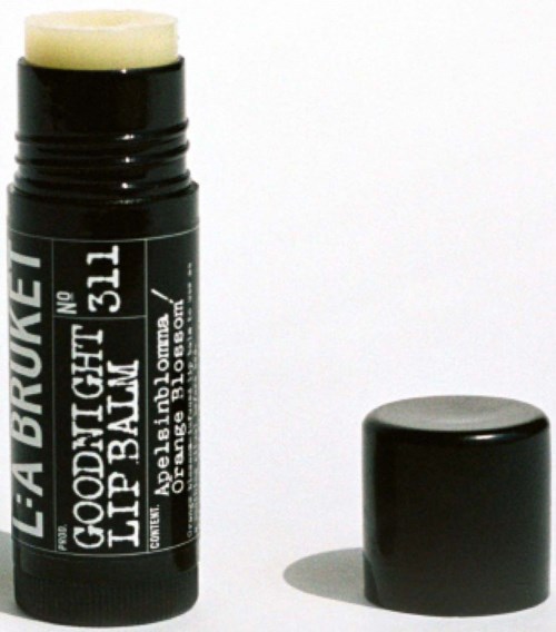 Ein schwarzer Lippenpflegestift mit weißem Etikett, neben seinem Deckel auf weißem Hintergrund.