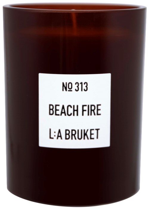 Eine dunkelbraune Kerze in einem Behälter, beschriftet 'Beach Fire'.