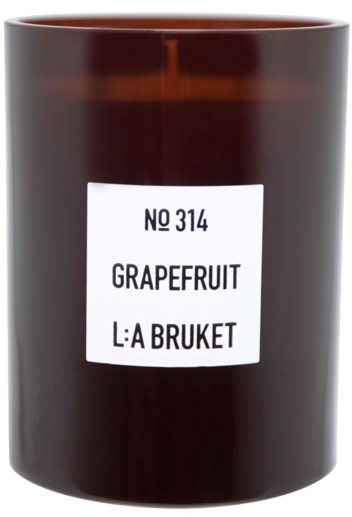 Eine dunkelbraune Kerze mit einem weißen Etikett, das Grapefruit-Duft und einen Produktnamen auf Schwedisch anzeigt.
