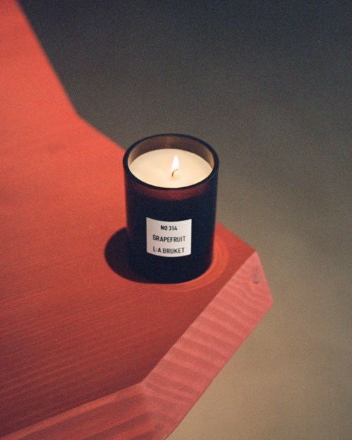 Eine schwarze Kerze mit einem Etikett liest 'Grapefruit La Bruket' auf einer Holztischkante.