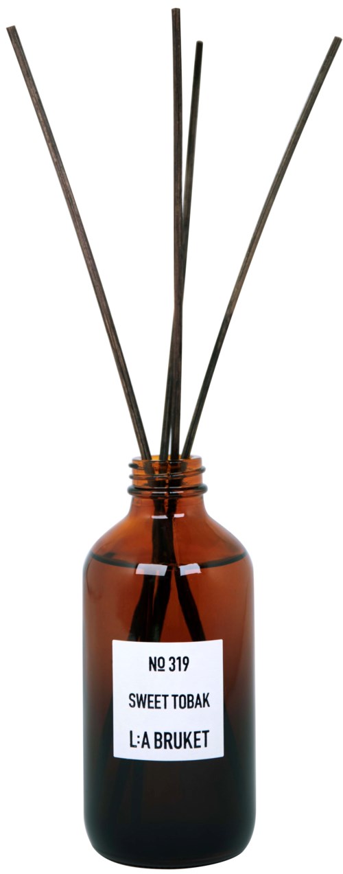 Een bruine fles met een wit label en zwarte reed-sticks erin, gebruikt als geurverspreider.