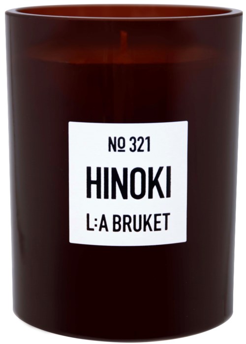 Een bruin kaars met een wit etiket waarop staat "HINOKI" en andere tekst, en een brandende lont bovenaan.