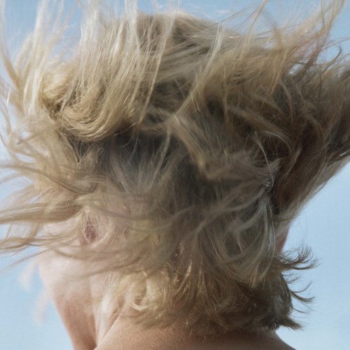 Haare wehen im Wind, Haarfarbe ist hell, und der Hintergrund ist klarer Himmel.