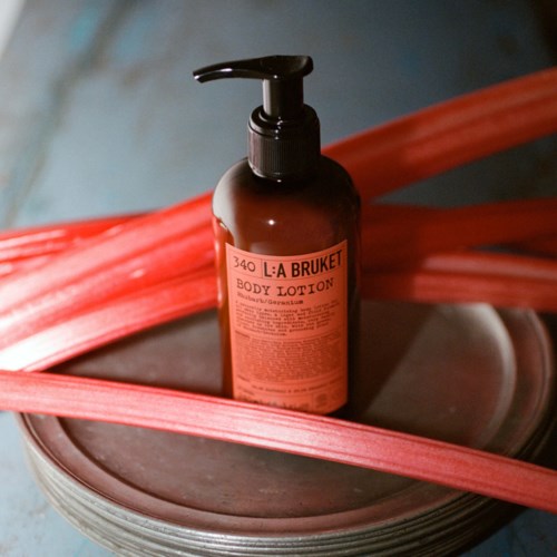 A brown bottle labeled L:A BRUKET body lotion with a pump, resting on a round tray with pink straps.