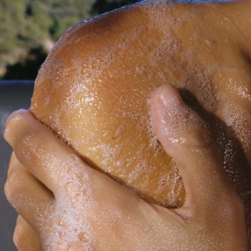 Eine Hand hält einen nassen, runden Donut mit knusprigen Rändern und Blasen an der Oberfläche.