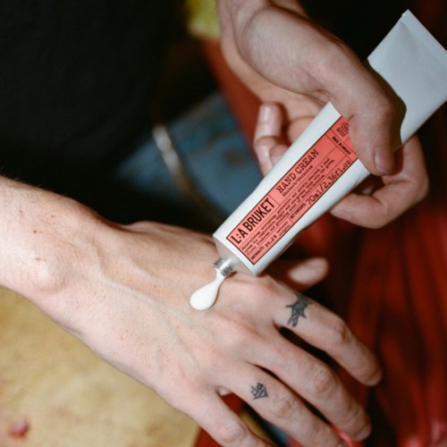Hand applying hand cream from a tube to another person's hand, with a casual background.