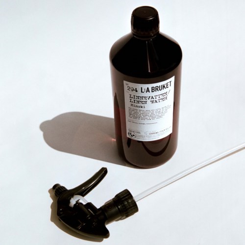 Eine dunkle Flasche mit 'L:A BRUKET Limevatten'-Aufdruck und Spraykopf, liegend auf weißer Oberfläche.